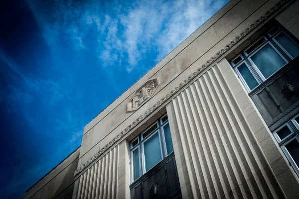 AN ANGLED IMAGE TAKEN UPWARD OF AN ORNATE GOVERNMENT BUILDING WITH A FLAT ROOF AND BLUE SKY