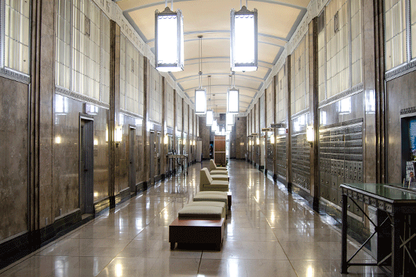 interior hallway with high ceiling with large lights suspended from the ceiling and furniture through the center of the hallway with walking space on either side of the hall. 