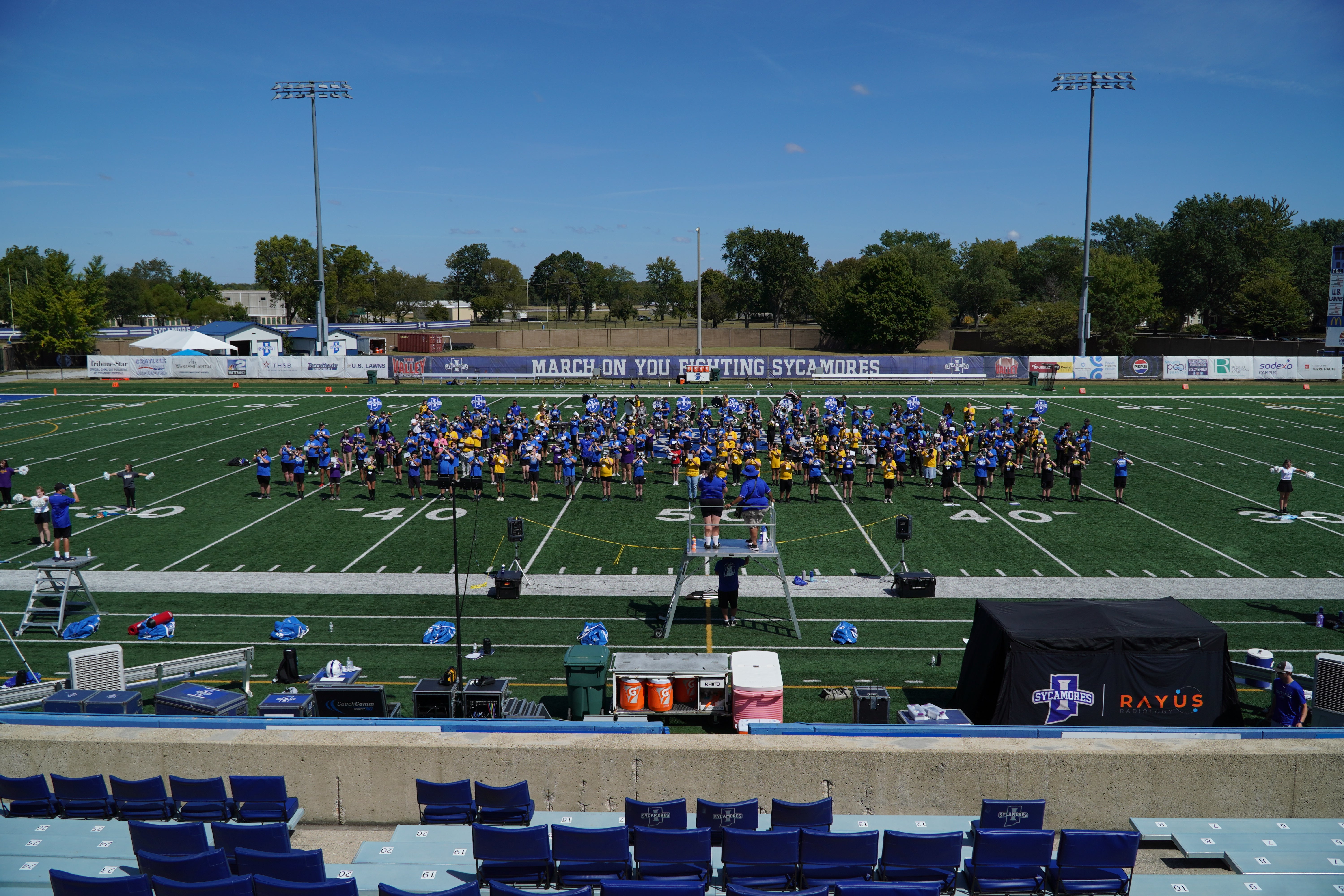 The Syacmore Marching Band on a football field, with bleachers and equipment in the foreground.