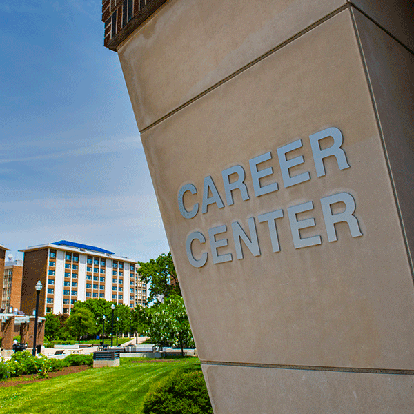 A building with the words “Career Center” prominently displayed on its exterior wall. In the background, there are other buildings, greenery, and a clear blue sky. 